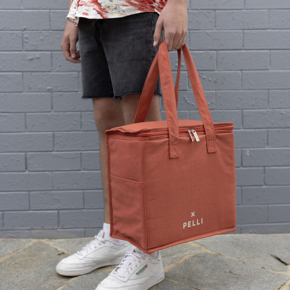 A person holding a medium cooler bag in clay by the straps
